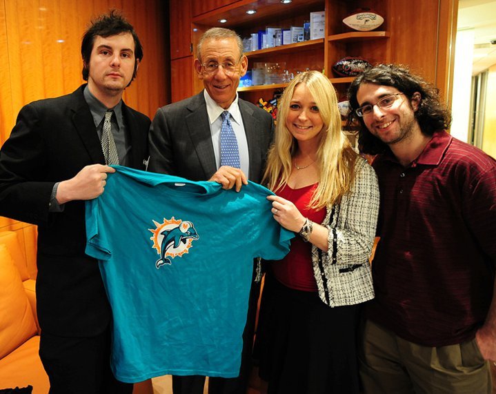 Miami Dolphins owner Stephen Ross holds up a DolfansNYC shirt with Igor, Michelle, and Alex.